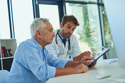 Buy stock photo Shot of a handsome doctor going over some paperwork with a male senior patient in a clinic