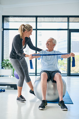 Buy stock photo Full length shot of a female physiotherapist helping a senior man stretch with a stretching band in a fitness centre