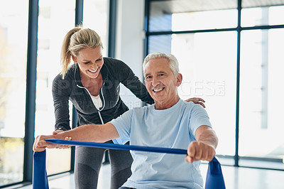 Buy stock photo Cropped shot of a female physiotherapist helping a senior patient stretch with a stretching band in a fitness centre