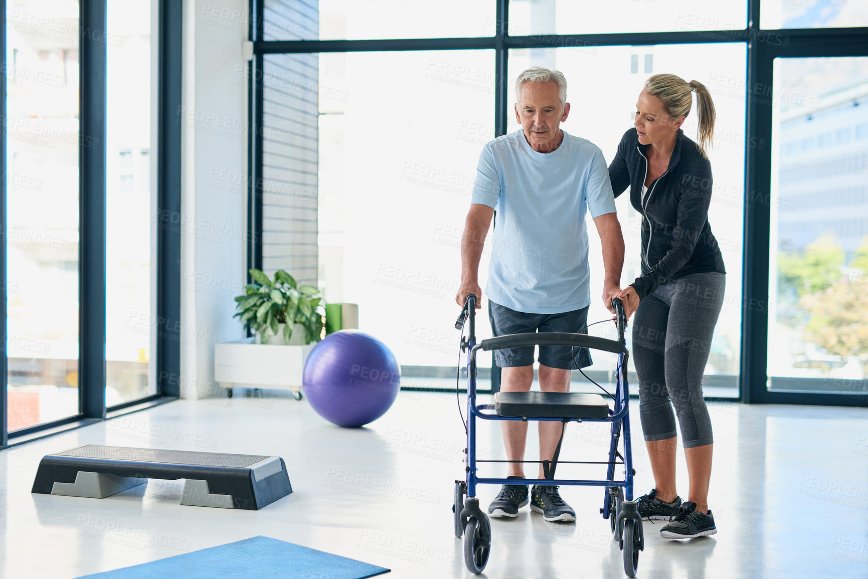 Buy stock photo Full length shot of a friendly female physiotherapist helping a senior use a walker in a fitness centre