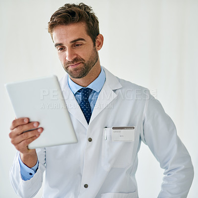 Buy stock photo Cropped shot of a handsome young doctor reading from a digital tablet in his office