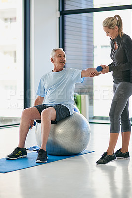 Buy stock photo Full length shot of a happy senior man working out with weights with the help of a physiotherapist