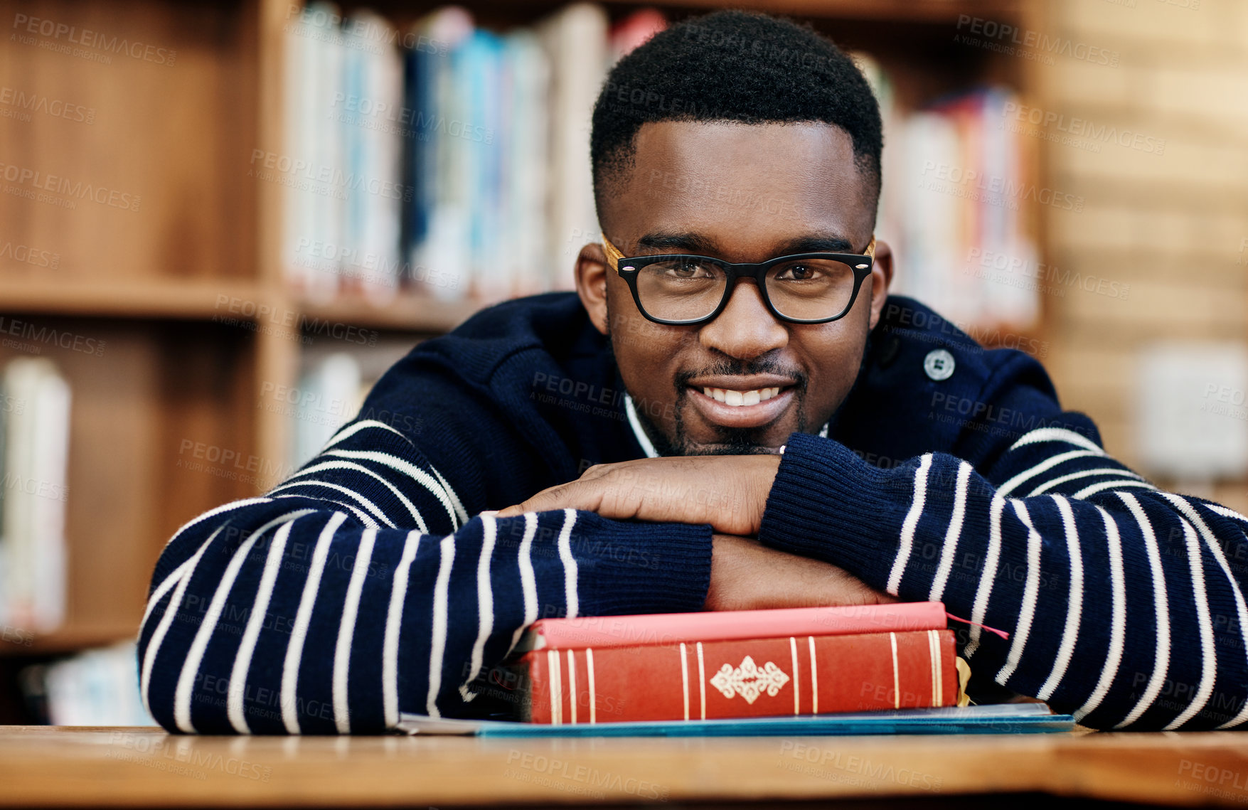 Buy stock photo African man, book and portrait at college, library and happy for studying, learning or development. Person, student and smile with laying at desk with research for assessment, exam or quiz in hall