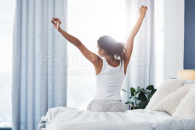 Buy stock photo Rearview shot of an unrecognizable young woman stretching while sitting on her bed in the morning