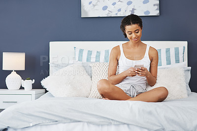 Buy stock photo Shot of an attractive young woman using her smartphone while sitting on her bed at home