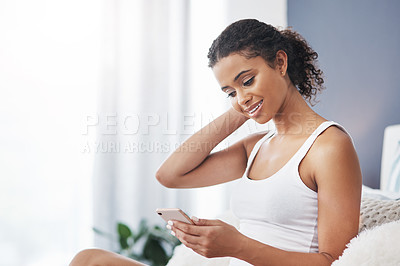 Buy stock photo Shot of an attractive young woman using her smartphone while sitting on her bed at home