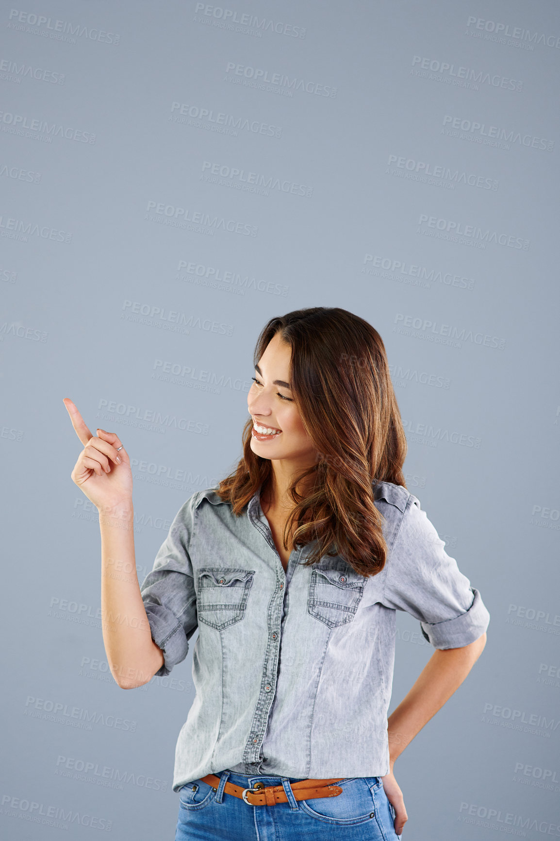 Buy stock photo Studio shot of an attractive young woman pointing towards copyspace against a grey background