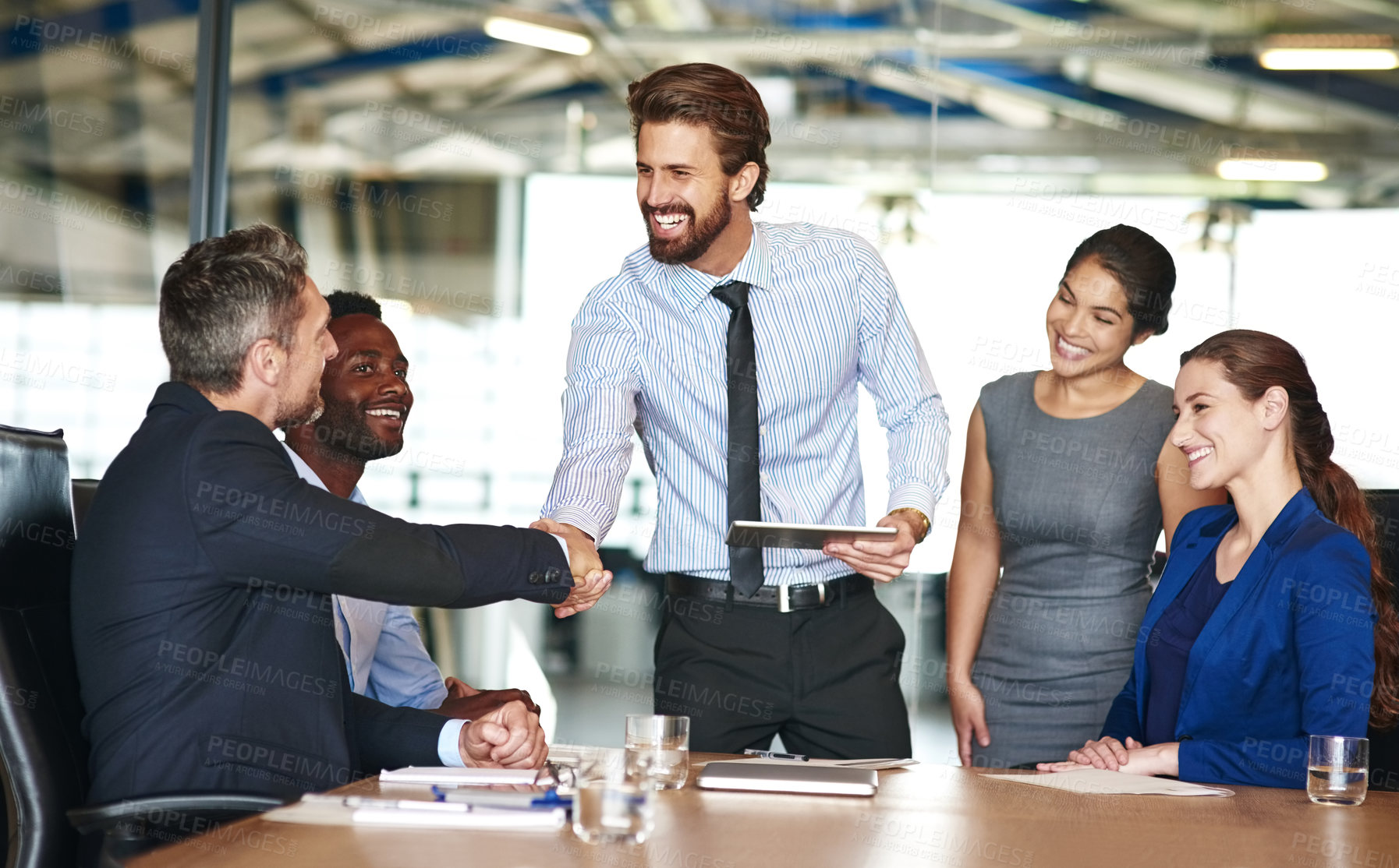 Buy stock photo Shot of two businesspeople shaking hands while in a meeting with colleagues