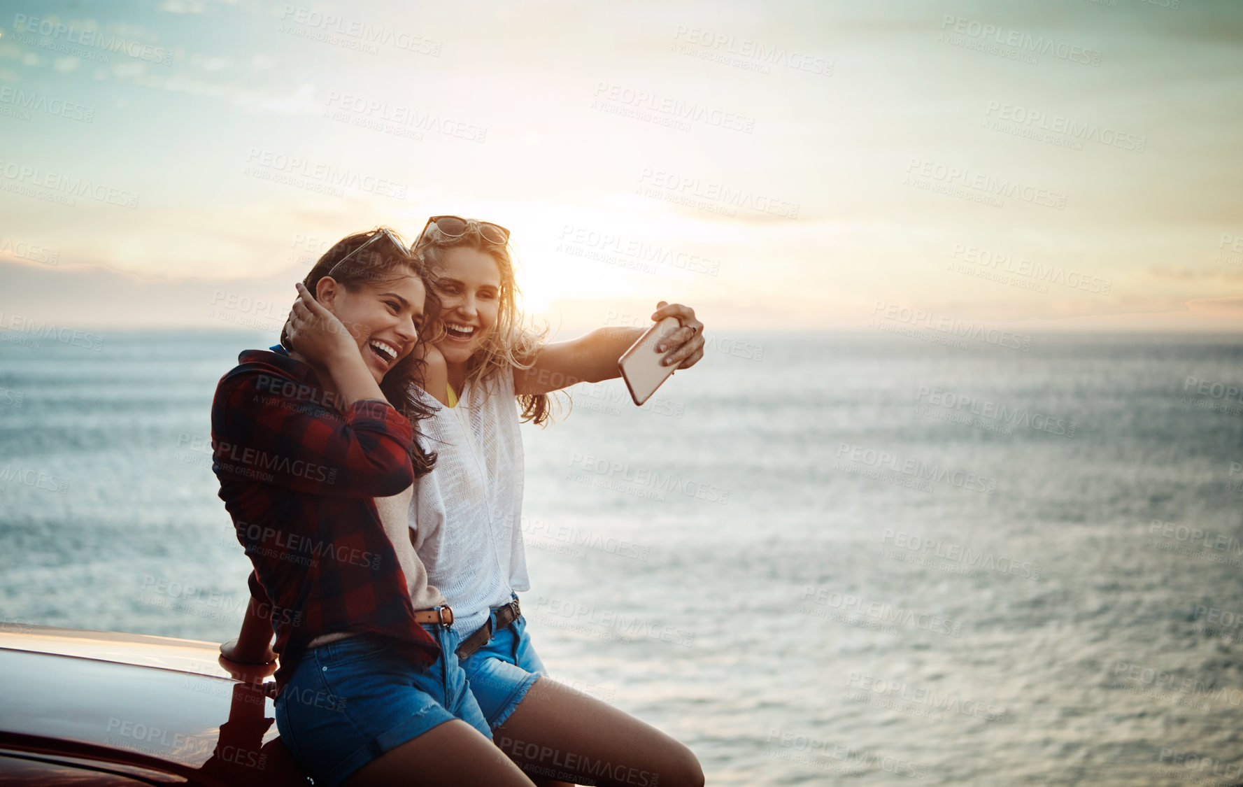Buy stock photo Shot of two friends taking a selfie with a smartphone on a summer’s road trip