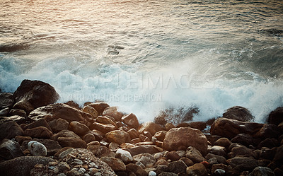 Buy stock photo Shot of water crashing against some boulders at the beach