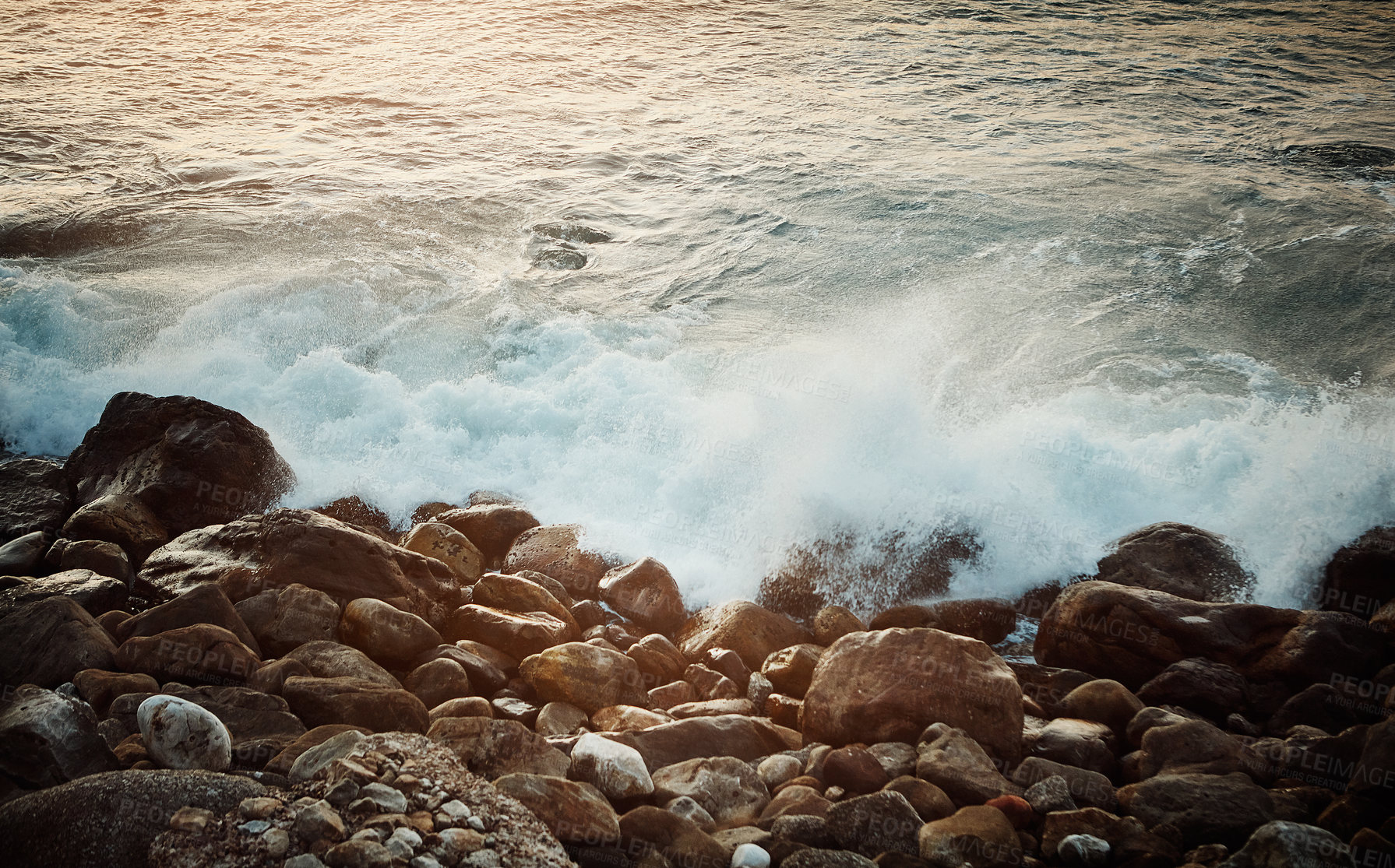 Buy stock photo Shot of water crashing against some boulders at the beach