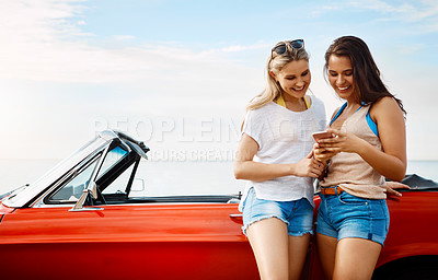Buy stock photo Shot of two friends using a smartphone on a summer’s road trip