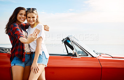 Buy stock photo Shot of two friends taking a selfie with a smartphone on a summer’s road trip