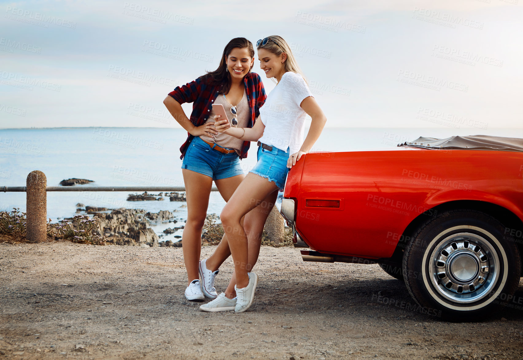 Buy stock photo Shot of two friends using a smartphone on a summer’s road trip