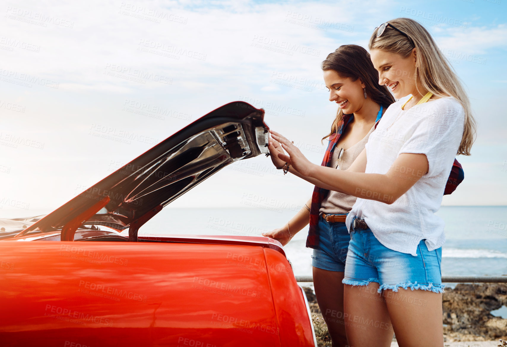 Buy stock photo Shot of two friends unpacking opening the trunk of their car on a summer’s road trip