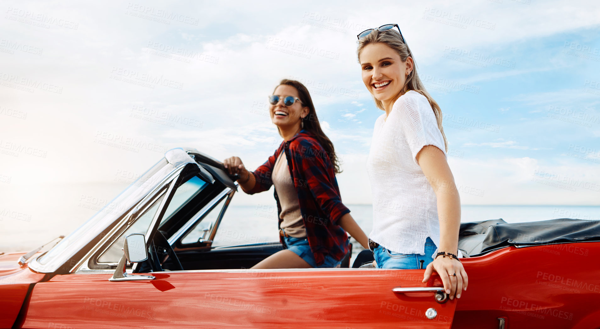 Buy stock photo Shot of a two happy young women enjoying a summer’s road trip together