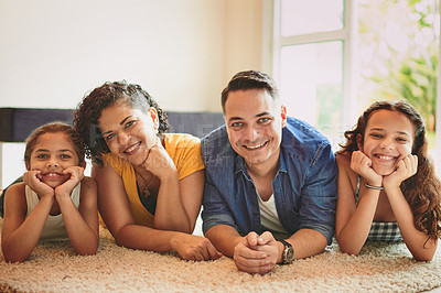 Buy stock photo Portrait of a family of four smiling at the camera while lying on the floor