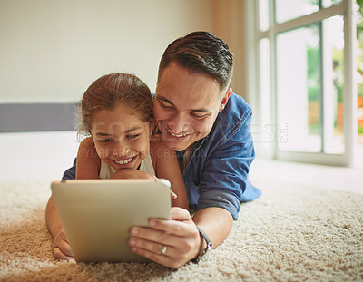 Buy stock photo Shot of a young girl and her father using a digital tablet while relaxing at home