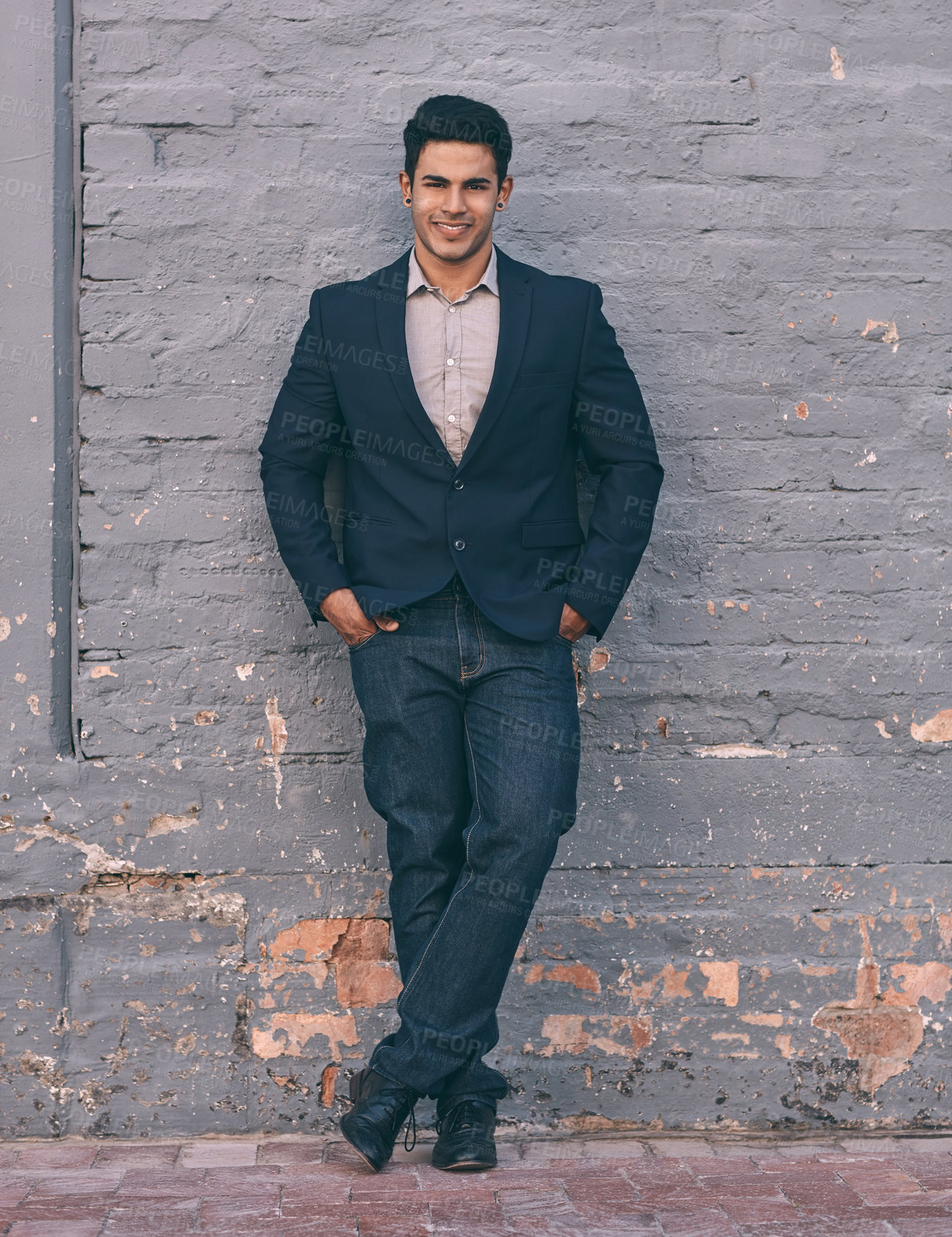 Buy stock photo Portrait of a handsome young businessman standing against a face brick wall with his hands in pockets