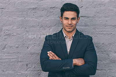 Buy stock photo Portrait of a handsome young businessman standing against a face brick wall with his arms folded