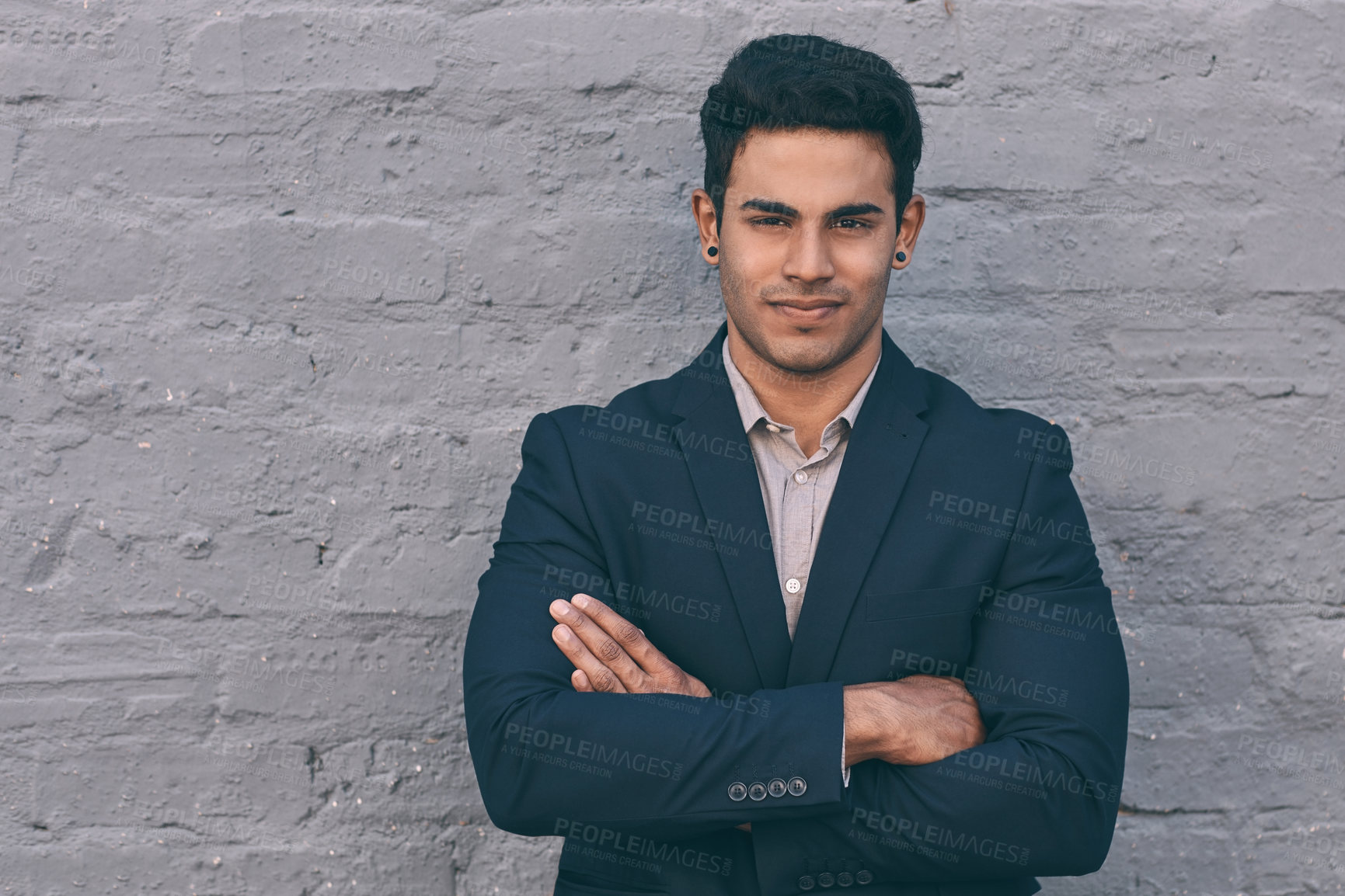 Buy stock photo Portrait of a handsome young businessman standing against a face brick wall with his arms folded