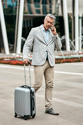 Buy stock photo Shot of a mature businessman talking on a cellphone while walking with a suitcase in the city