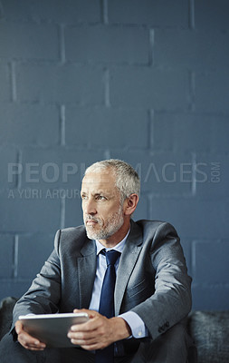 Buy stock photo Cropped shot of a handsome and thoughtful mature businessman using a digital tablet in his office