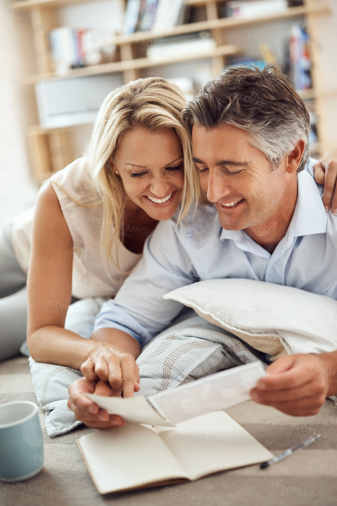 Buy stock photo Cropped shot of an affectionate mature couple lying on their living room floor looking at photographs