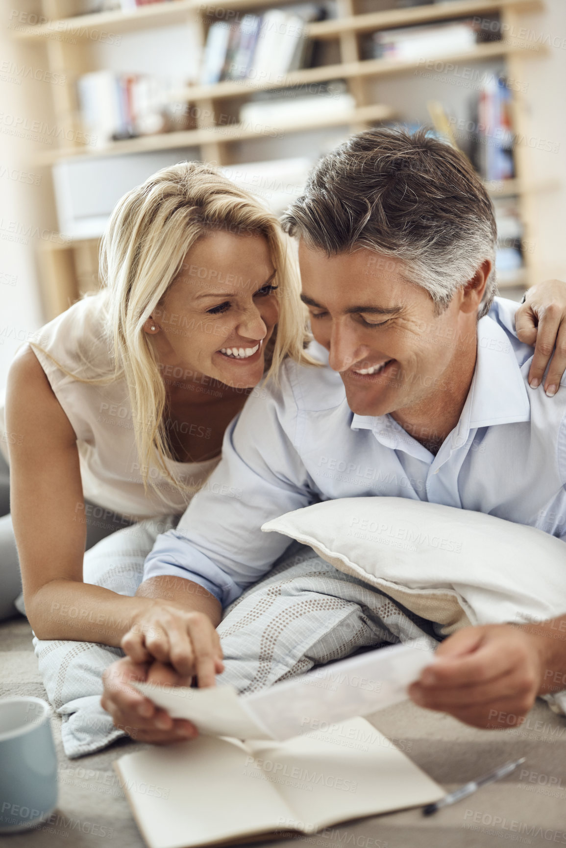 Buy stock photo Cropped shot of an affectionate mature couple lying on their living room floor looking at photographs