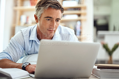 Buy stock photo Cropped shot of a handsome mature man lying on his living room floor using a laptop