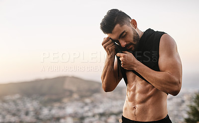 Buy stock photo Shot of a sporty young man wiping the sweat from his forehead with his top while exercising outdoors