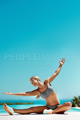 Buy stock photo Shot of a young attractive woman stretching with her arms outstretched after her workout by the pool on a sunny day