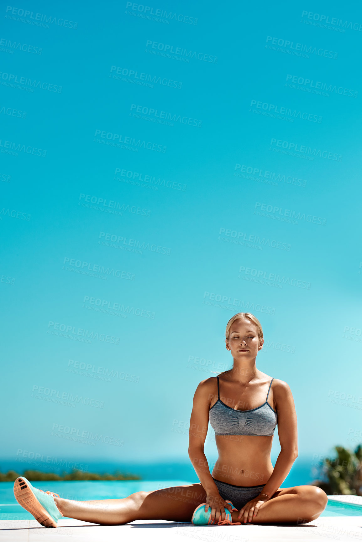 Buy stock photo Shot of a young attractive woman in workout gear stretching her legs after her workout by the pool