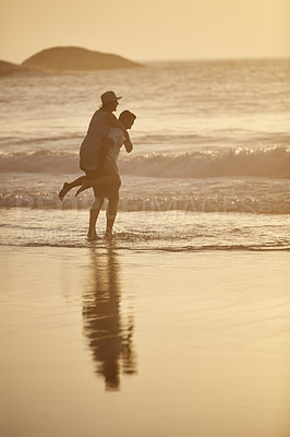 Buy stock photo Shot of a man piggybacking his girlfriend on the beach