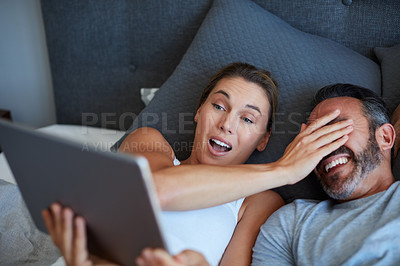 Buy stock photo High angle shot of an attractive young woman covering her husband's eyes while holding a digital tablet