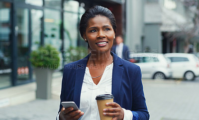 Buy stock photo Shot of an attractive young businesswoman holding her cup of coffee and a cellphone while out in the city