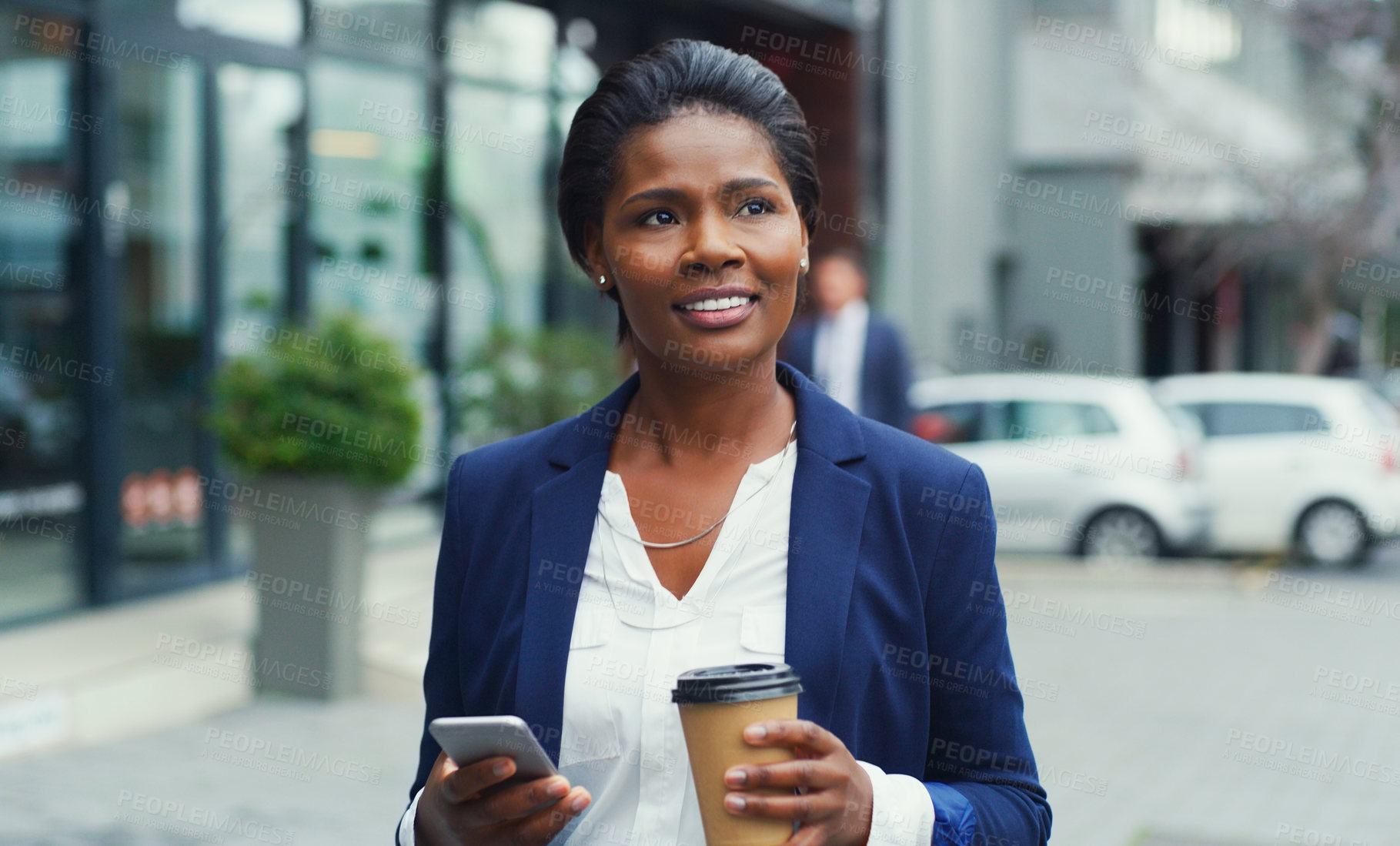 Buy stock photo Shot of an attractive young businesswoman holding her cup of coffee and a cellphone while out in the city