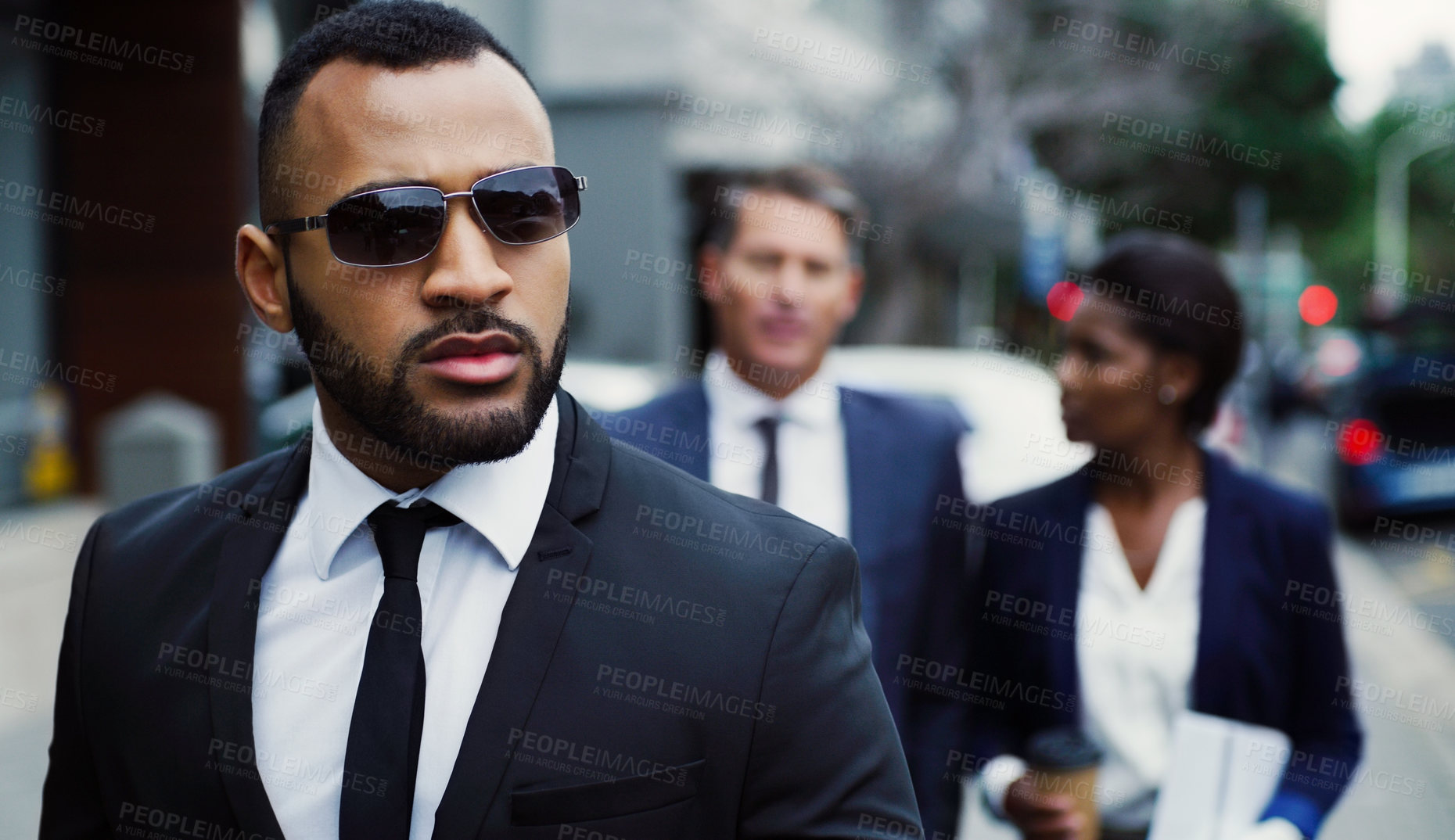 Buy stock photo Shot of a handsome young businessman walking in the city with his colleagues behind him in the background