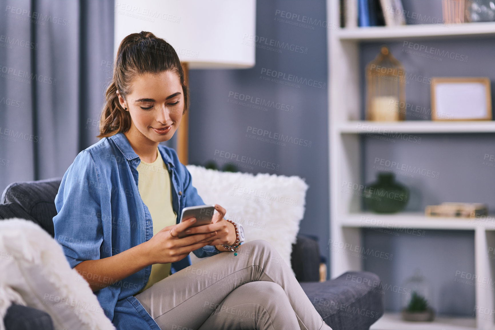 Buy stock photo Shot of a beautiful young woman using a cellphone while relaxing on a couch at home