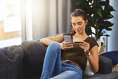 Buy stock photo Shot of a beautiful young woman using her cellphone and credit card to do some online shopping at home