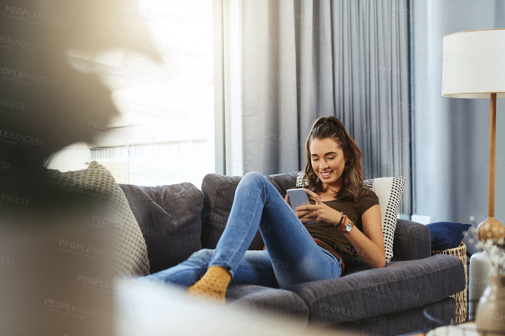 Buy stock photo Shot of a beautiful young woman using a cellphone while relaxing on a couch at home