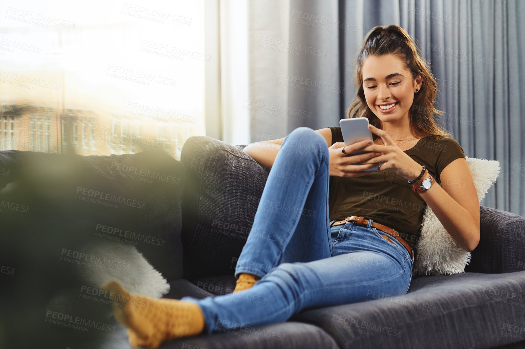 Buy stock photo Full length shot of a beautiful young woman using a cellphone while relaxing on a couch at home