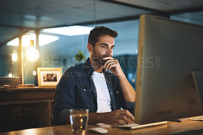 Buy stock photo Shot of a handsome young businessman working late at night on his computer in a modern office