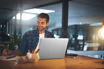 Buy stock photo Shot of a handsome young businessman smiling while working late at night on his computer in a modern office