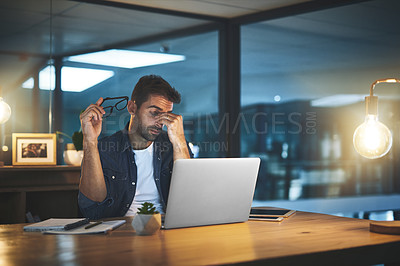 Buy stock photo Shot of a handsome young businessman feeling stressed while working late at night in a modern office