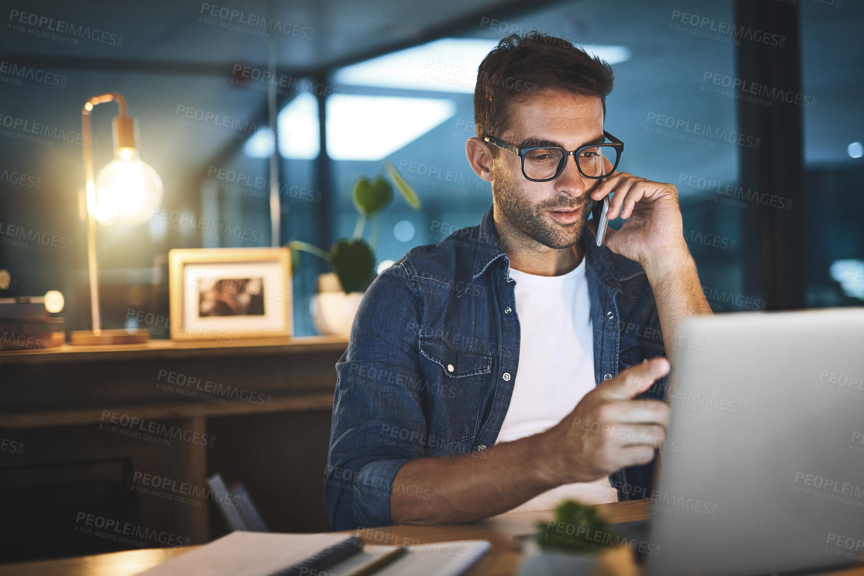 Buy stock photo Shot of a handsome young businessman talking on his cellphone while sitting at his desk in a modern office