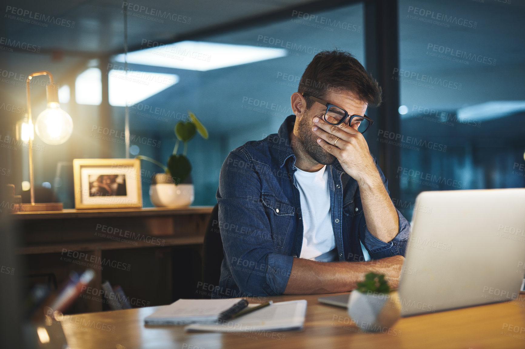 Buy stock photo Shot of a handsome young businessman feeling stressed while working late at night in a modern office