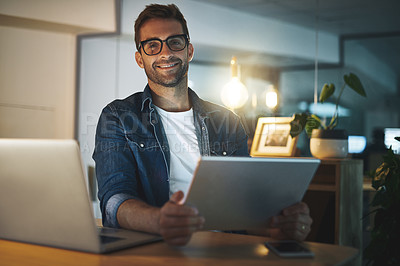 Buy stock photo Portrait of a handsome young businessman smiling while working late at night on his tablet in a modern office