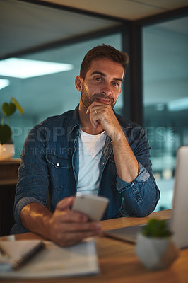 Buy stock photo Portrait of a handsome young businessman using his cellphone while sitting at his desk in a modern office