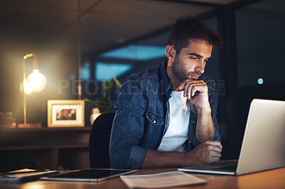 Buy stock photo Shot of a handsome young businessman working late at night on his computer in a modern office